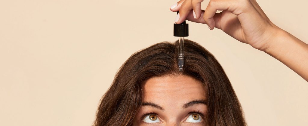 Woman applying scalp serum to roots with dropper